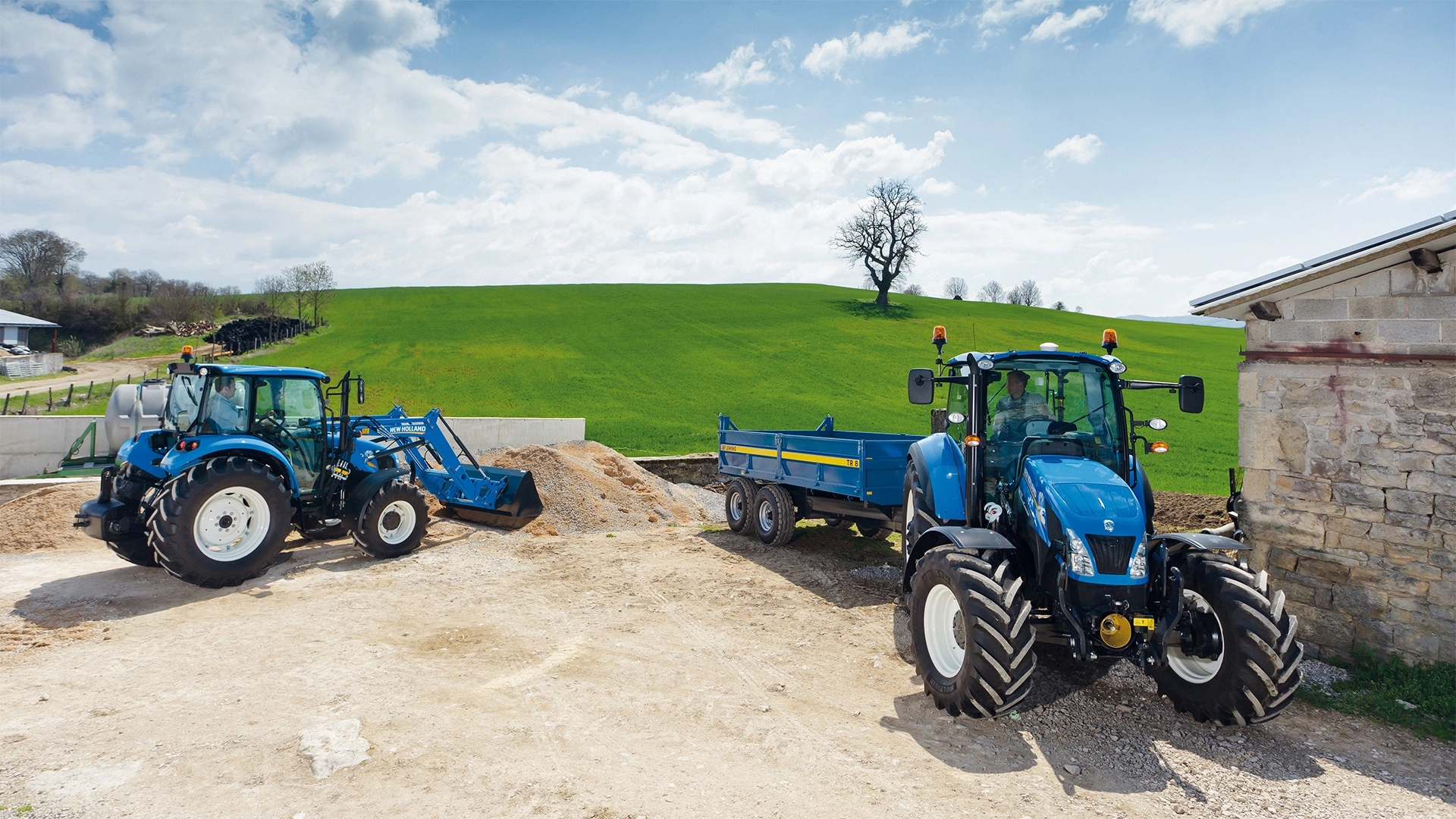 Two New Holland T4 tractors are in a work area. One tractor has a front loader, and the. other tractor has a blue trailer mounted on it. The background features a green hill with a lone tree and a partly cloudy sky.