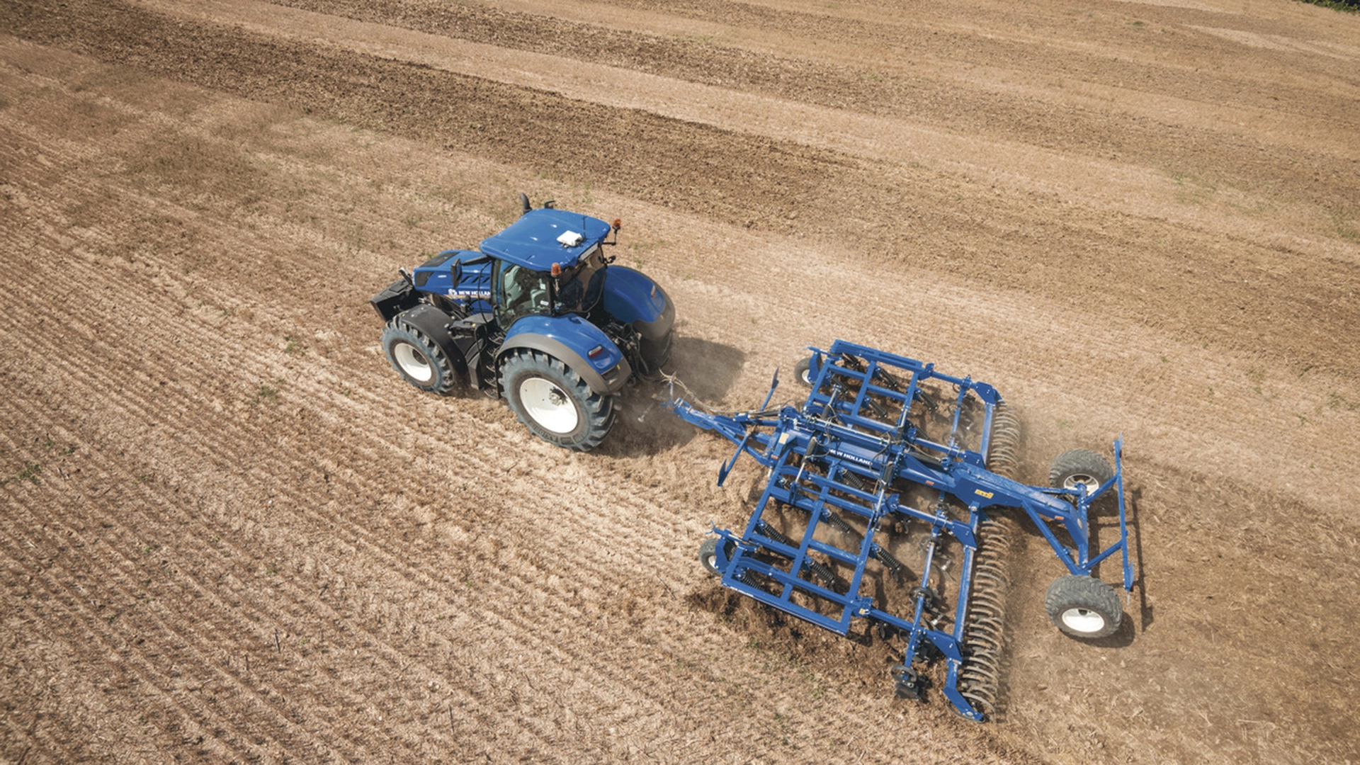 New Holland tractor employing a mounted stubble cultivator with Spring Tine Cultivator, discs and rear rollers on the field
