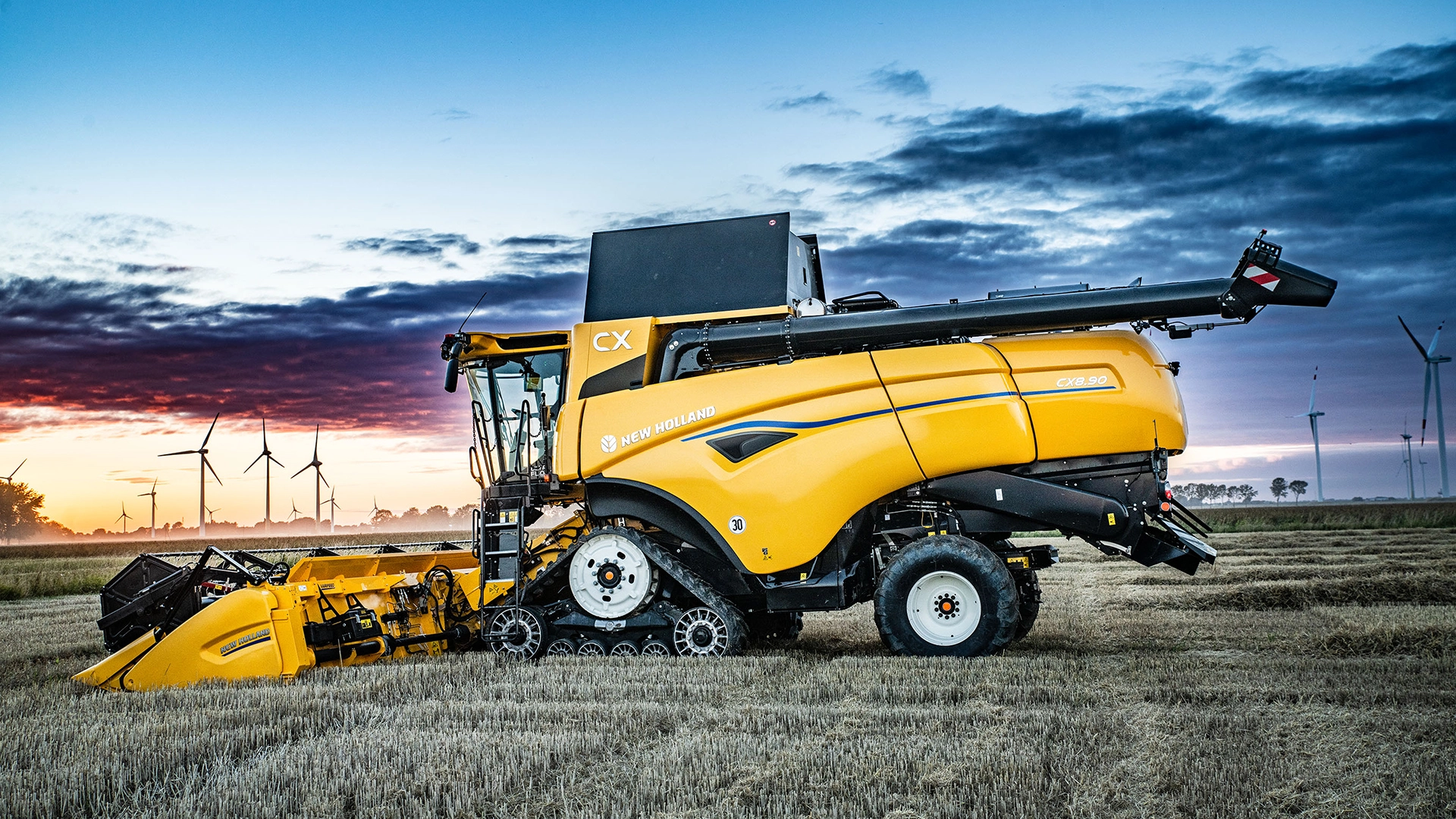 New Holland CX7 & CX8 combine harvester, specifically the CX8.90 model, stationed in a field during sunset. 
