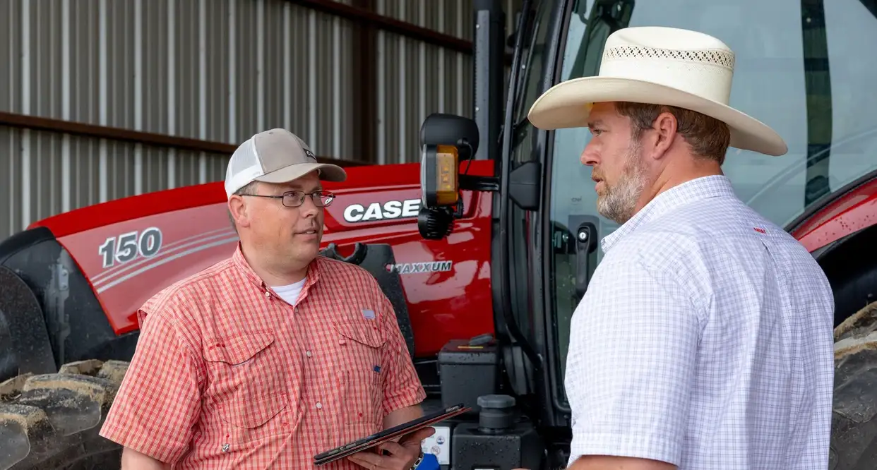 Dealer representative discussing farm connectivity technology with a farmer, standing in front of a Case IH Maxxum 150 tractor.