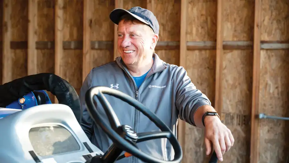 Cliente New Holland sorridente ao lado de seu trator, representando a confiança nas soluções da CNH Capital Corretora de Seguros.