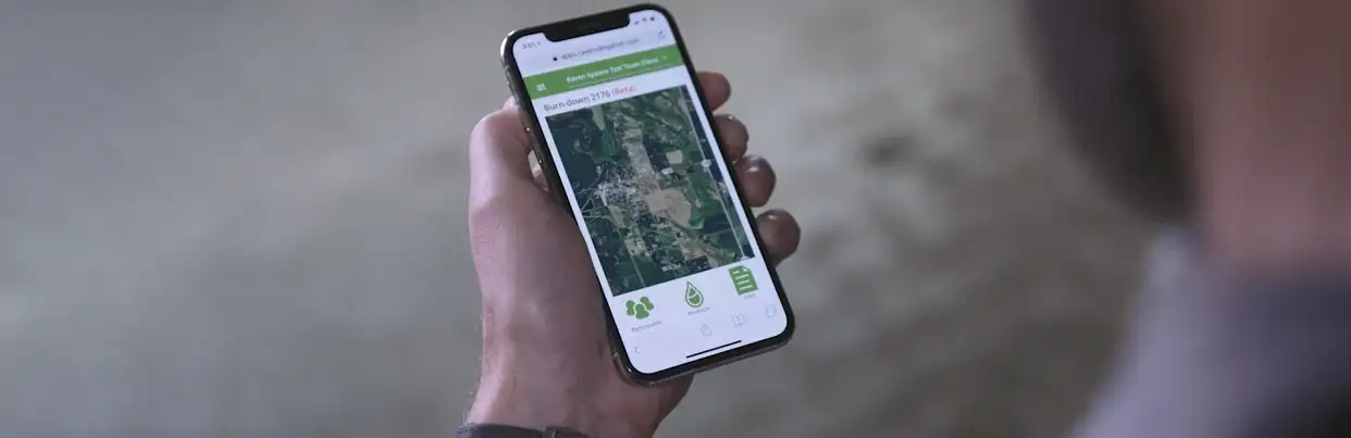 A person holds a smartphone displaying Slingshot with visible icons, suggesting navigation or agriculture planning in a neutral setting.