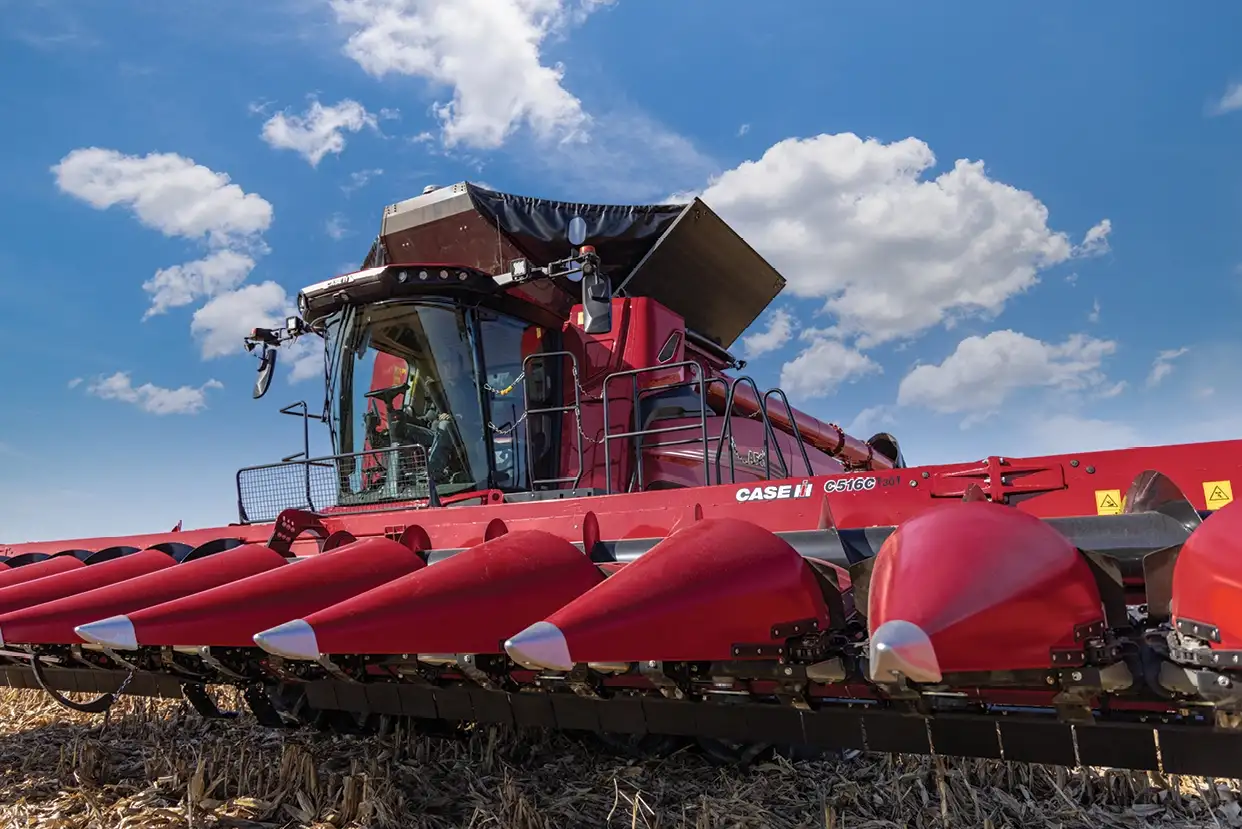 A Case IH C500 series combine harvester in a cornfield under a blue sky with fluffy clouds. 