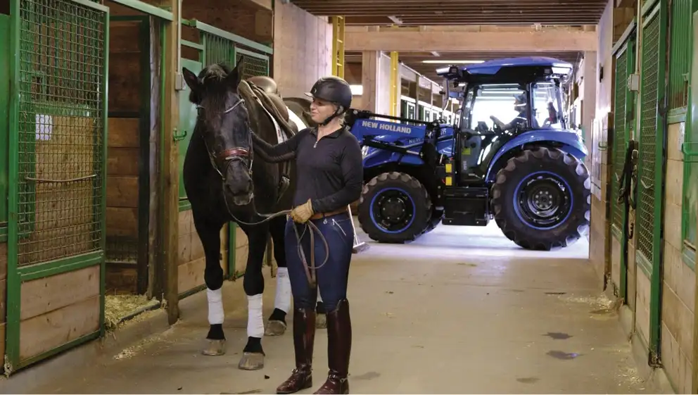 Woman stands with horse in front of New Holland electric tractor