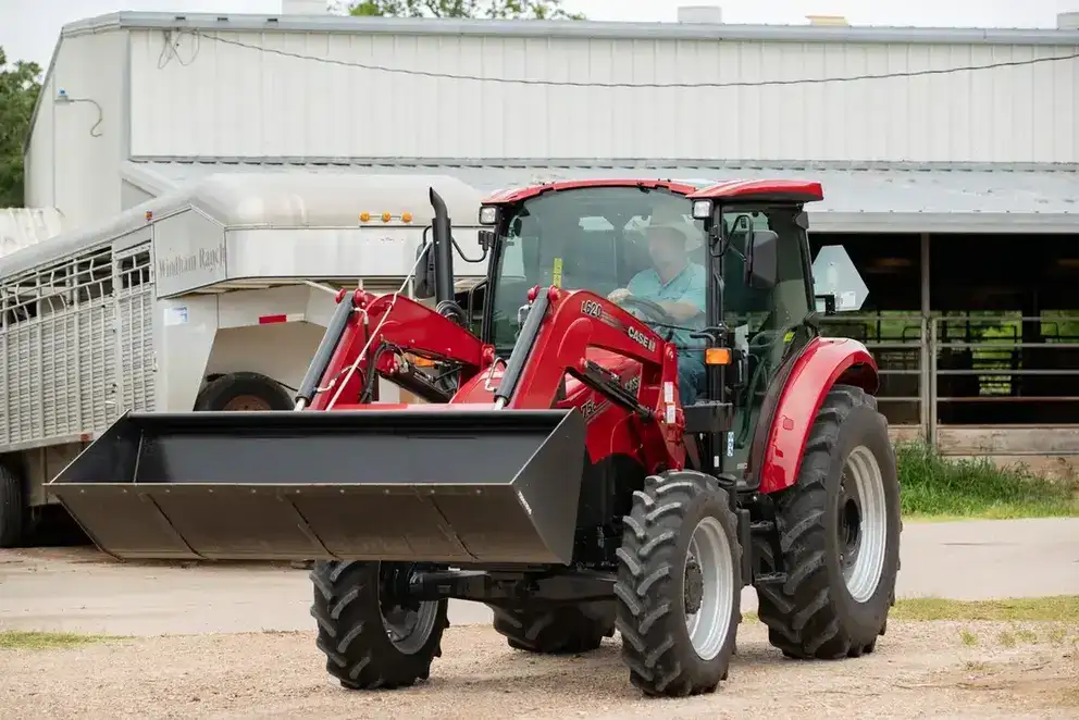 A Case IH tractor with large front loader parked in front of a metal barn. A person sits inside the cab. 