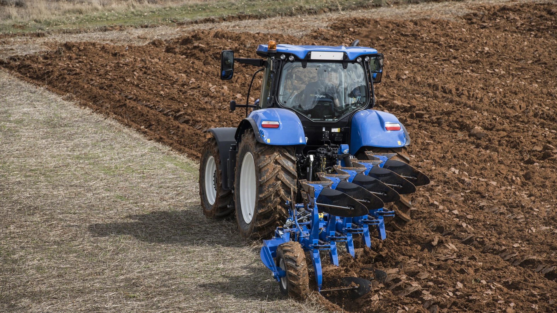Tractor with New Holland's 5 furrow fully-mounted variable width reversible plough working on the field