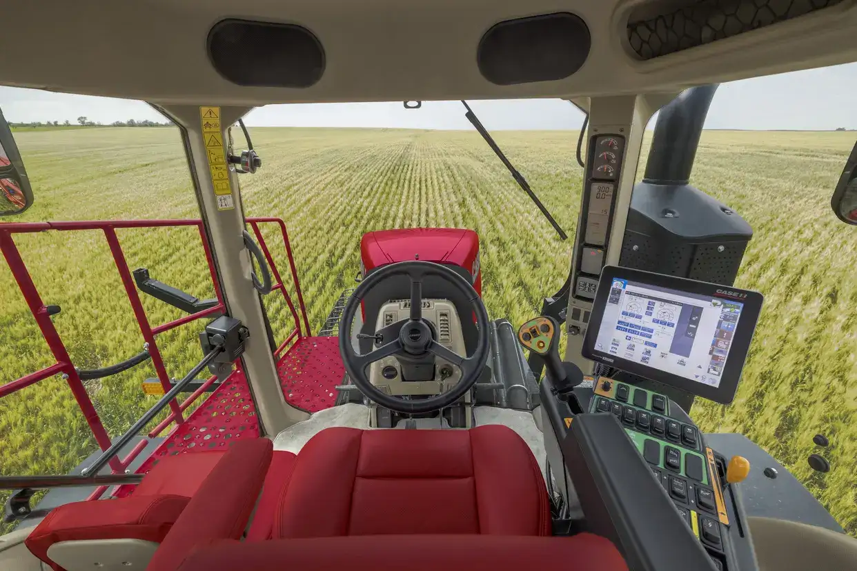 Interior view of a Case IH Trident cab with red seats and a steering wheel, looking out onto a vast, green field. A touchscreen display shows controls.