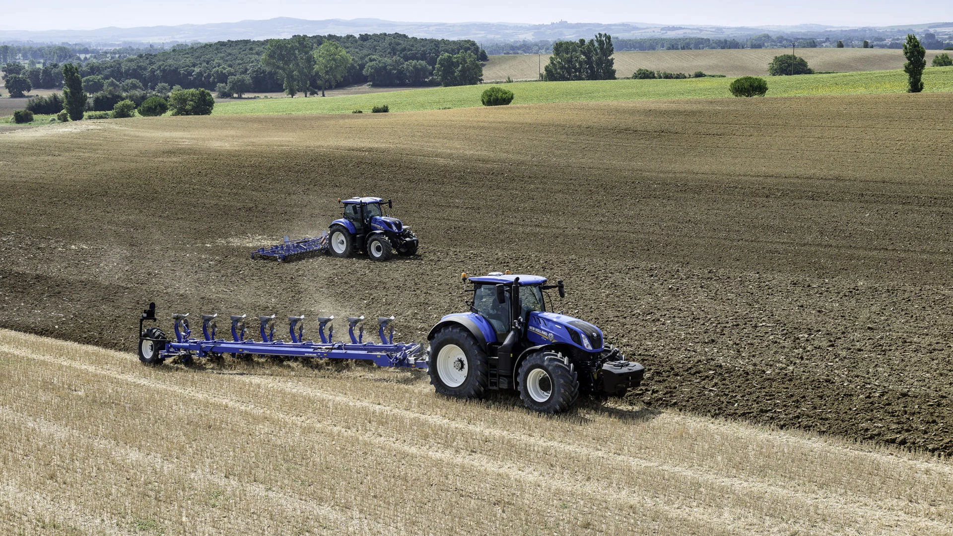 New Holland tractors with ploughing equipment on a field.