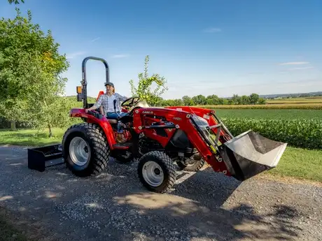 A person on a Case IH Compact 40A tractor in a rural landscape with green fields and blue sky, exuding a peaceful, productive farming atmosphere.