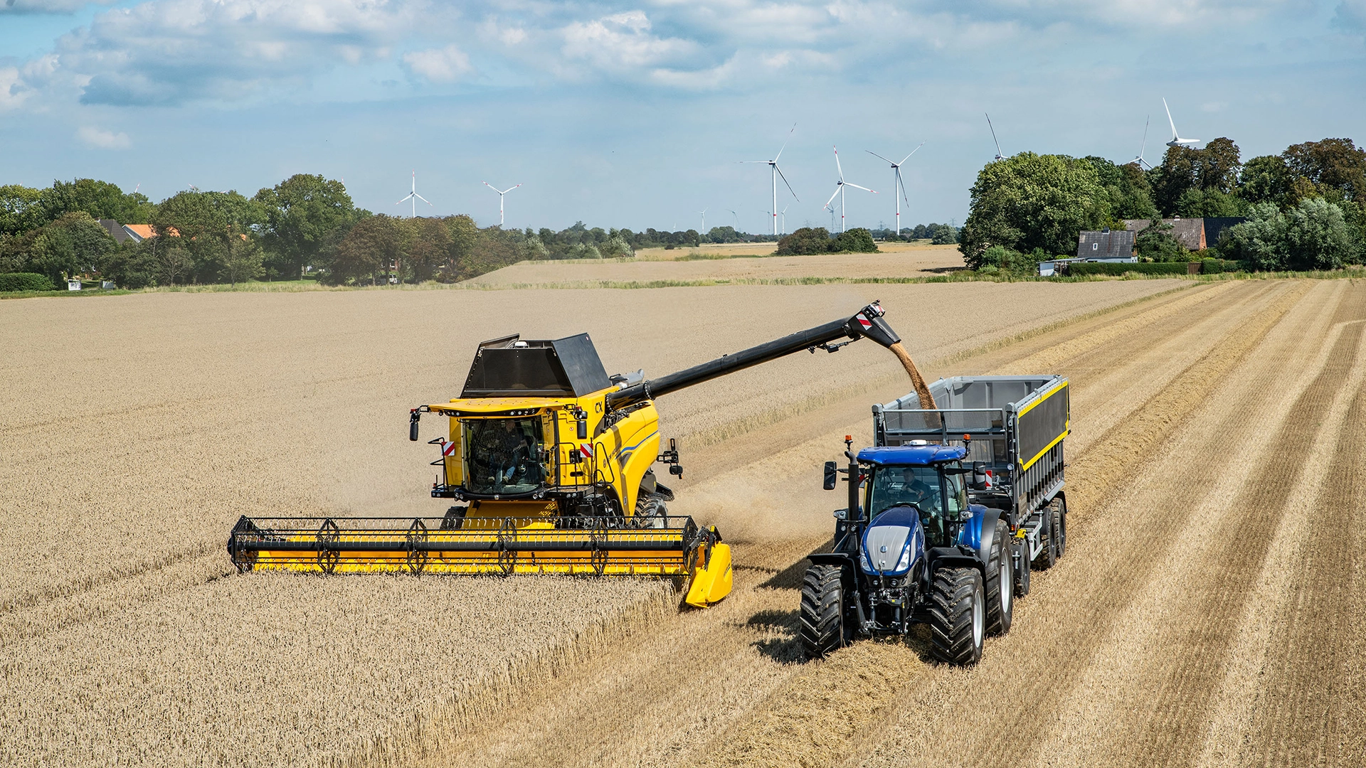 New Holland CX7 & CX8 combine harvester in action, transferring harvested grain into a trailer attached to a blue New Holland tractor.