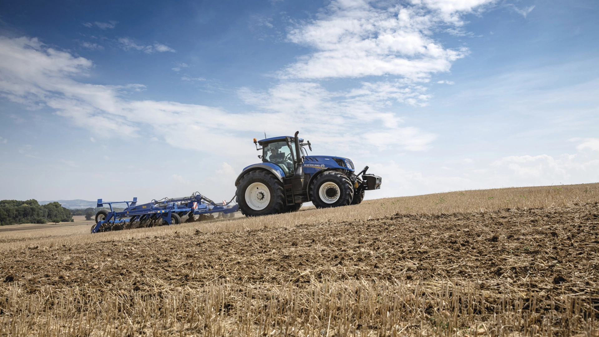 New Holland tractor employing a mounted stubble cultivator with rigid tine cultivator, discs and rear rollers on the field