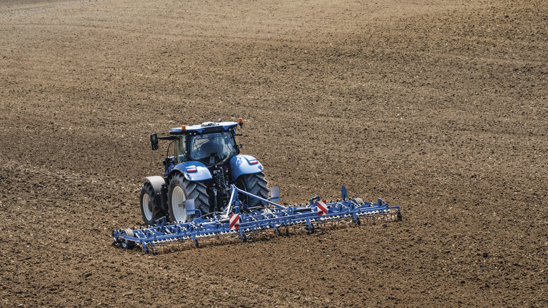 Agricultural scene of New Holland tractor and seedbed cultivators in action on the field