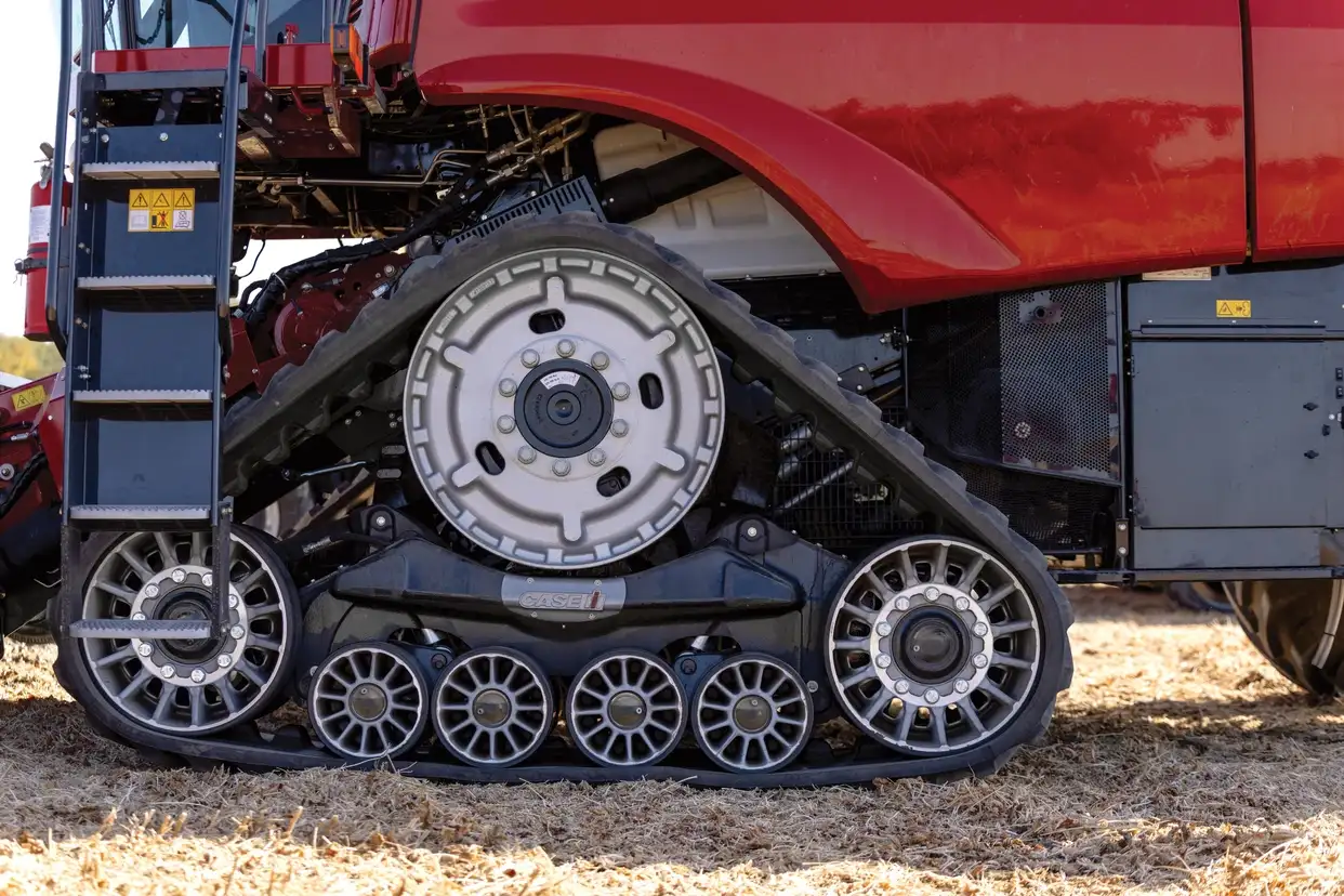 A close-up of the black rubber track system on a red Case IH combine harvester, featuring a large drive wheel and several smaller idler wheels on dirt.