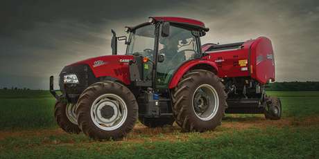 A woman driving a Case IH Farmall utility tractor which is pulling a Case IH round baler through a field.