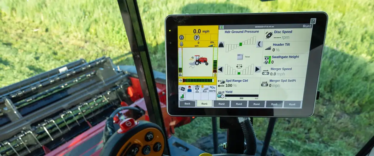 Inside a modern Case IH farm machine cab, a touchscreen displays harvesting data beside steering controls and red equipment in a sunny field.