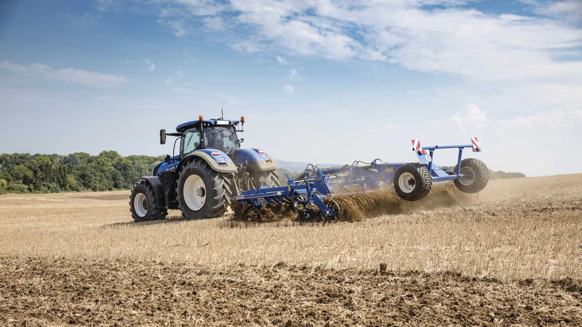 New Holland tractor employing a mounted stubble cultivator with rigid tine cultivator, discs and rear rollers on the field