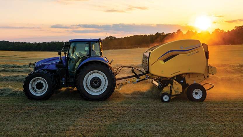 Tractor pulls yellow hay baler in a field.