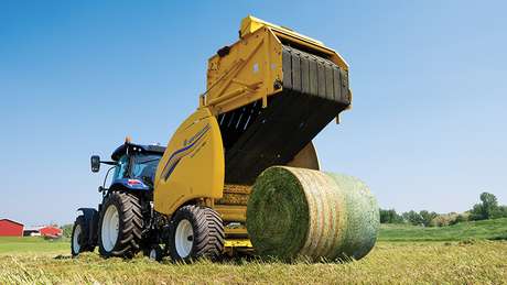 Tractor pulls yellow hay baler in a field.