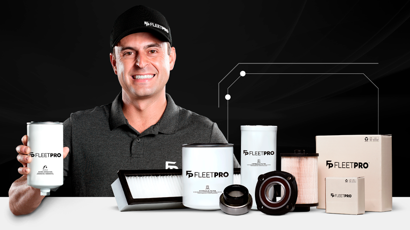 Homem uniformizado segurando filtro FleetPro, com diferentes modelos da linha FleetPro expostos sobre a mesa, incluindo filtros de óleo, ar e combustível.