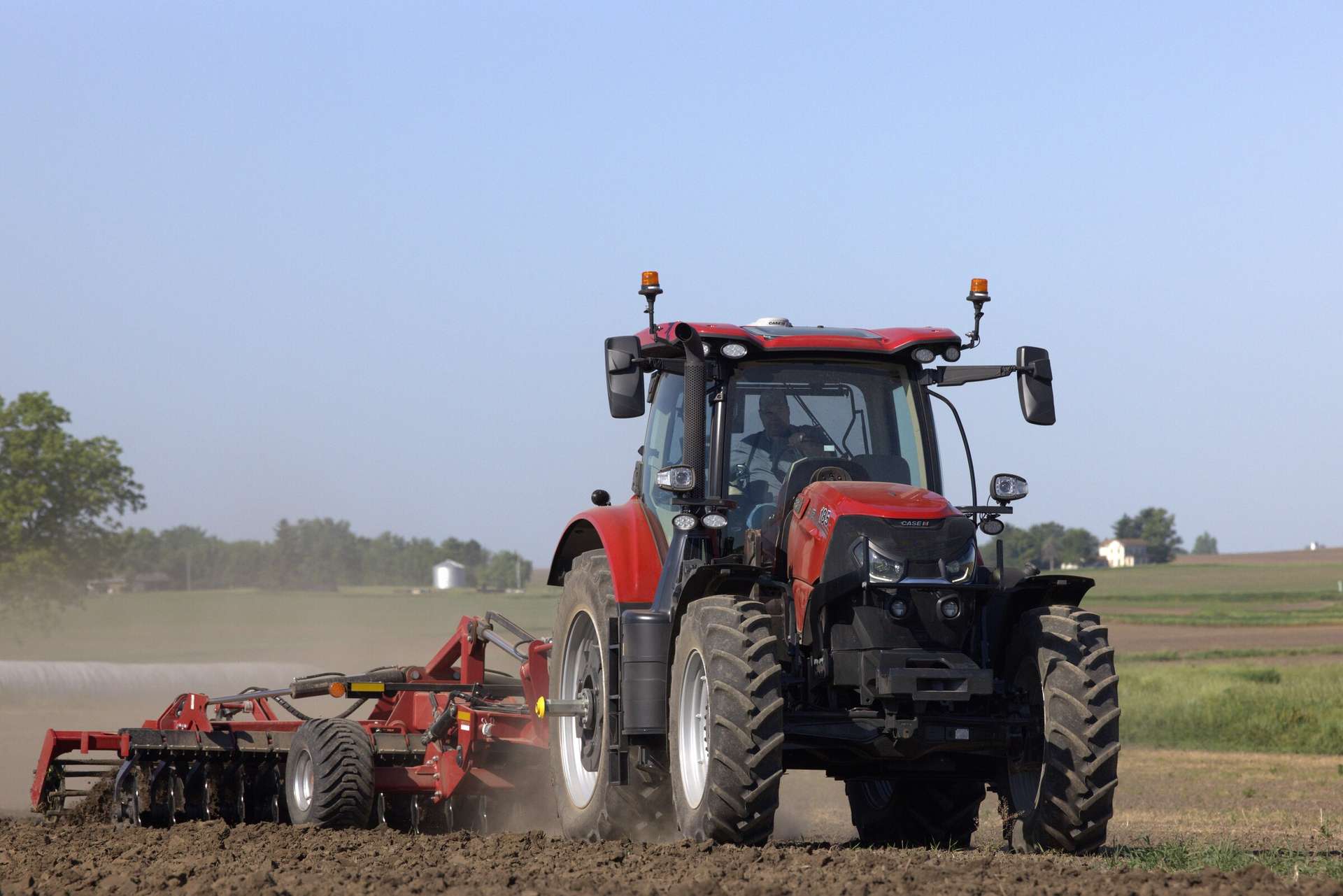 A Case IH tractor plows a vast, earthy field under a clear blue sky, evoking a sense of rural productivity and calm. 