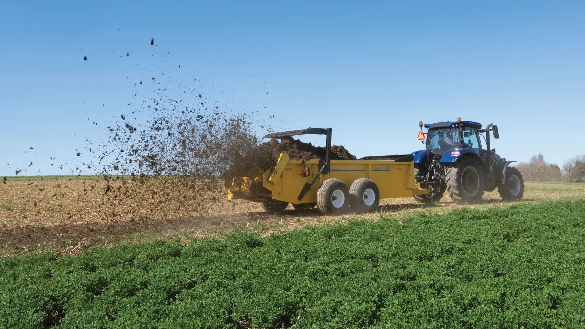 Yellow box spreader flings manure onto a field.