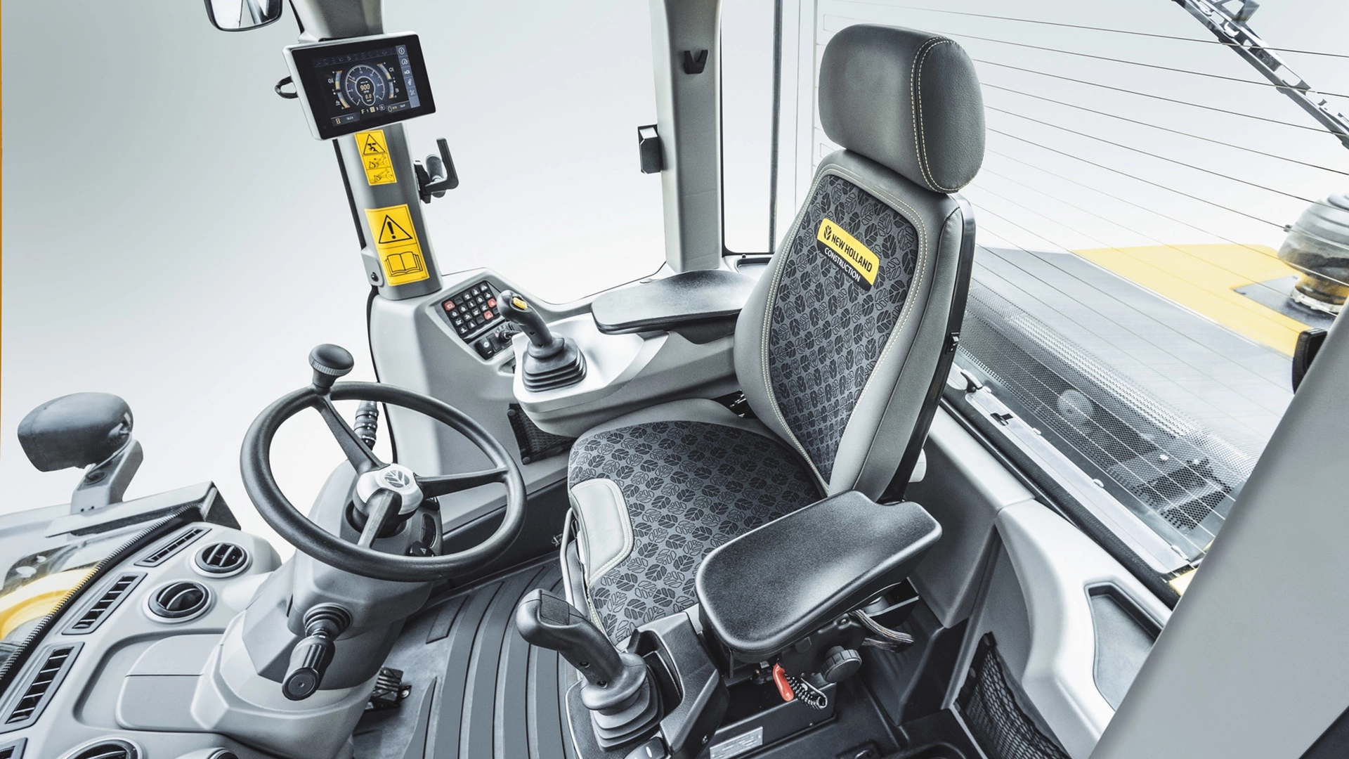 Interior view of a New Holland wheel loader cabin featuring ergonomic operator's seat, modern control panel, and digital display for efficient machine handling.