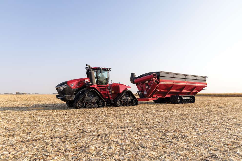 Red Case IH tractor attached to a large red grain cart on a harvested dry cornfield under a clear sky.