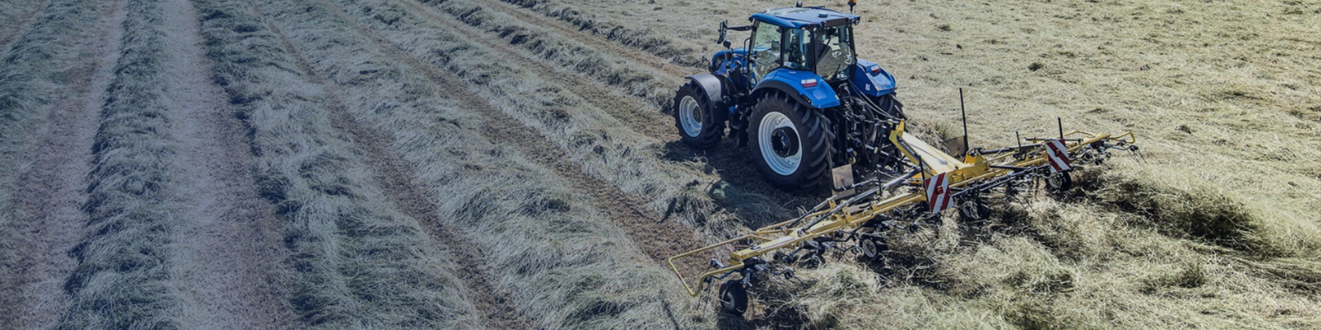 New Holland Tedders product working in field with New Holland tractor towing it