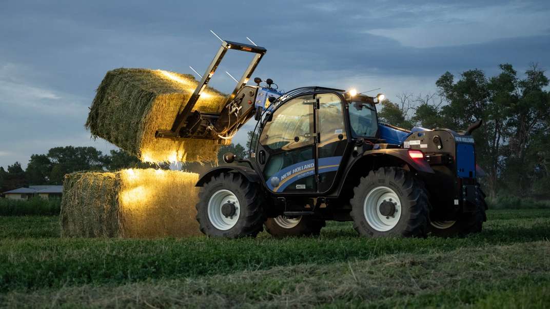 TH7.42 Plus Telehandler lifting hay bales at dusk.
