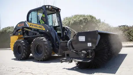 New Holland Construction L320 with a broom in a street.