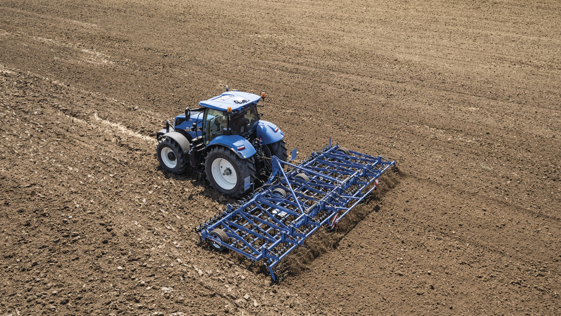 Active New Holland tractor with spring tine cultivators and cage roller tilling the soil