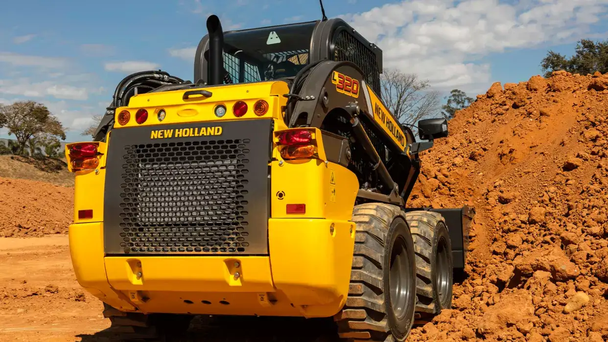 foto ao ar livre, da minicarregadeira New Holland Construction em operação, com destaque para a traseira.    
