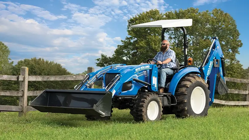 Man operates New Holland compact tractor with loader.