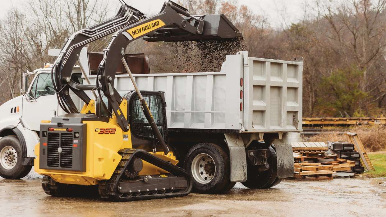 Compact track loader dumping dirt into a truck.