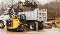 Compact track loader dumping dirt into a truck.
