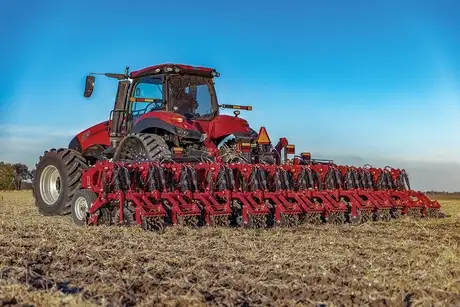 A Case IH tractor pulling a 12-row Nutri-Tiller 1030 folding-mounted toolbar through a harvested field. 