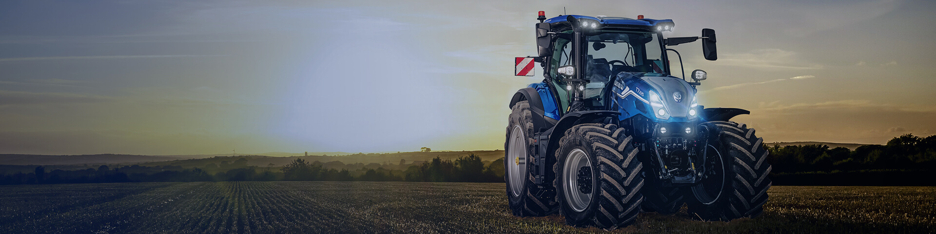 Blue New Holland new T7 SWB tractor sitting in field with sunset backdrop
