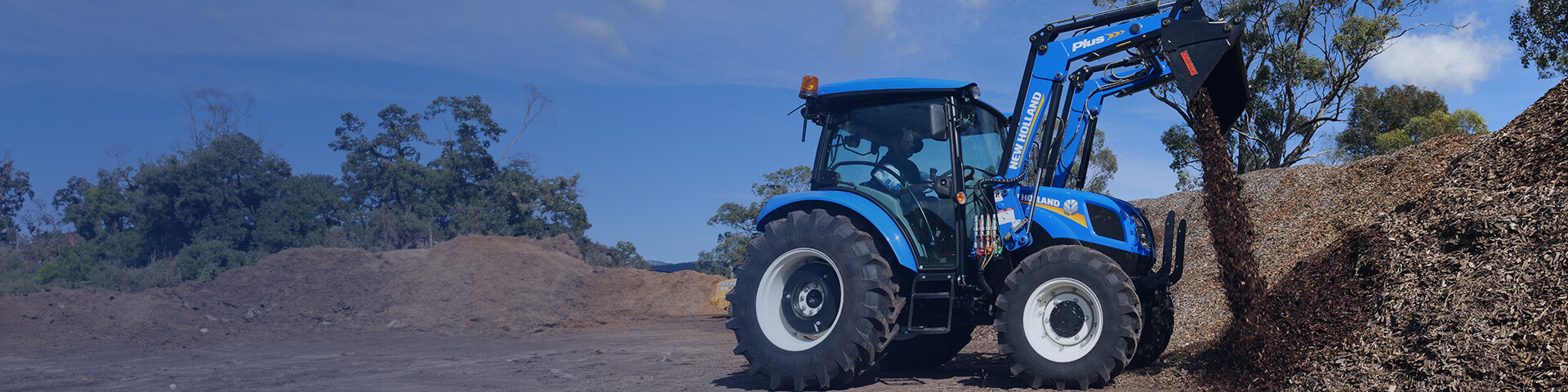 Blue New Holland TT4 Tier 3 tractor in field with loader and 4 in 1 bucket attached