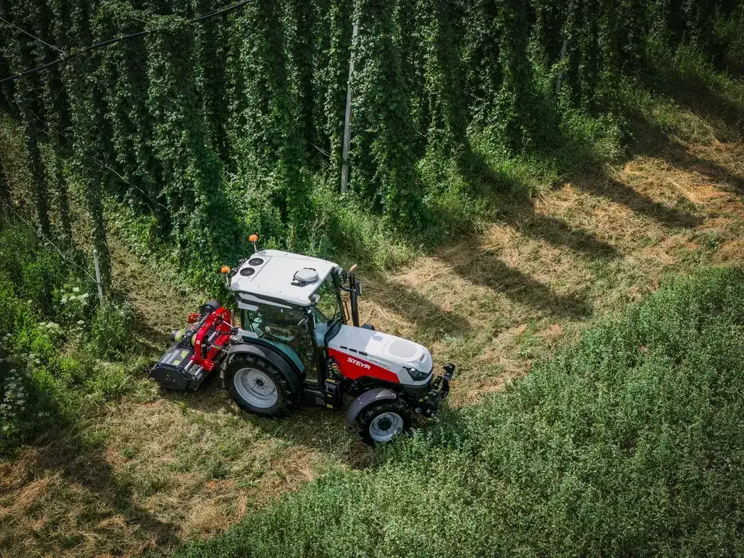 Luftaufnahme eines STEYR Spezial Traktors mit rotem Mulchgerät neben einer Hopfenanlage