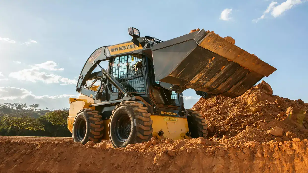 foto ao ar livre, da minicarregadeira New Holland Construction em operação, sobre um monte de terra. 