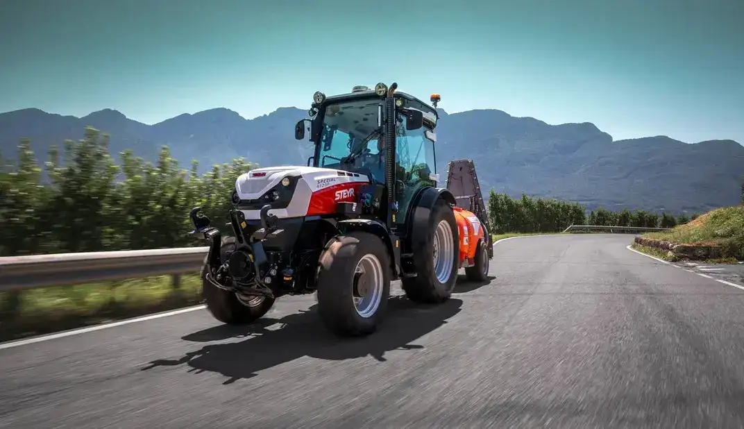 STEYR Spezial Obstbautraktor zieht ein Sprühgerät auf einer Bergstraße