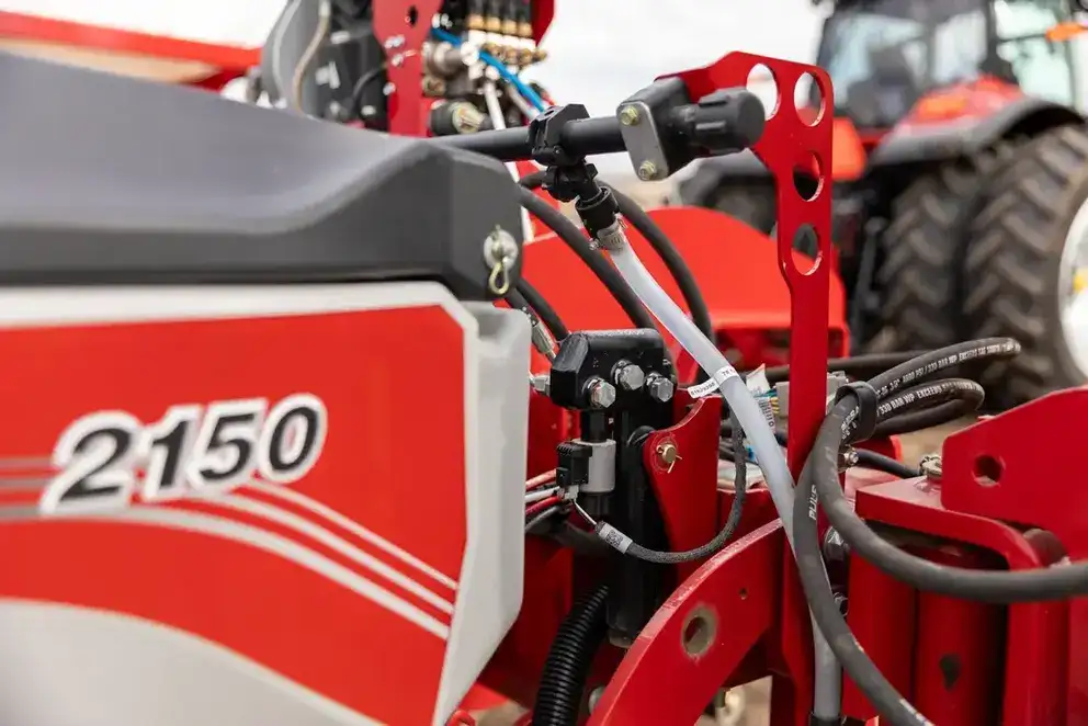 Close-up of red Case IH 2150 hydraulic connections. A tractor with large tires is visible in the background.