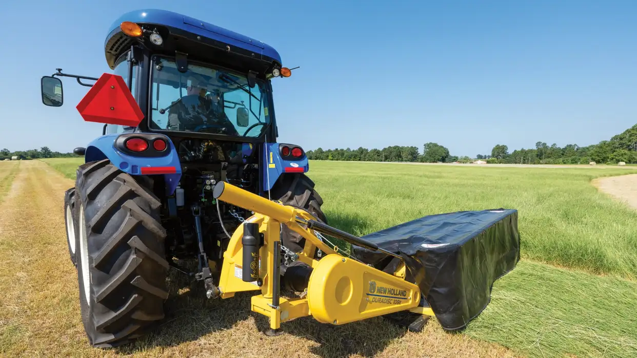 New Holland tractor pulling disc mower in field.
