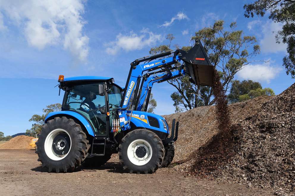 Blue New Holland TT4 Tier 3 tractor in field with loader and 4 in 1 bucket attached