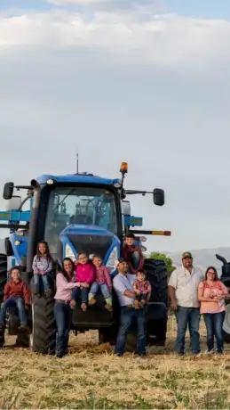 Family of 11 in front of a New Holland tractor in a field.