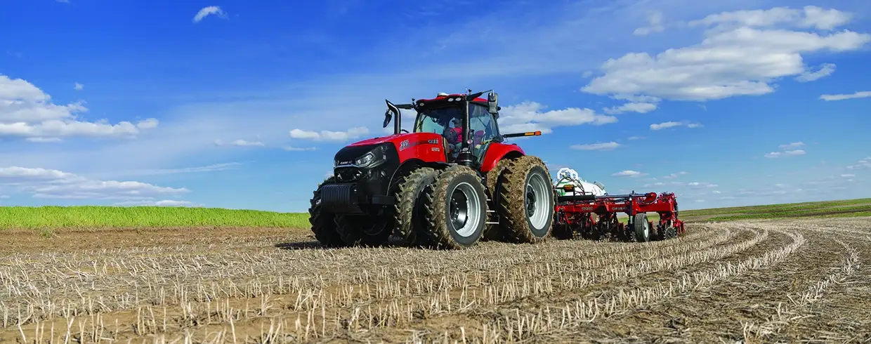 Red Case IH tractor with large tires plowing a harvested field under a blue sky with scattered clouds.