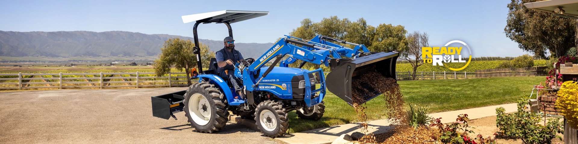 Operator uses WORKMASTER compact tractor with bucket to spread mulch.