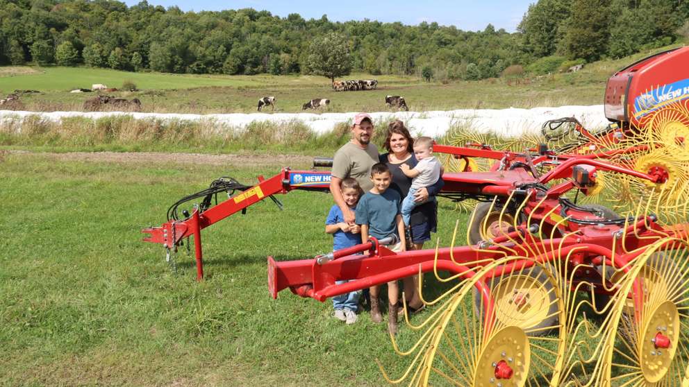 Family of 4 sit in front of New Holland Hay Rakes and cows.