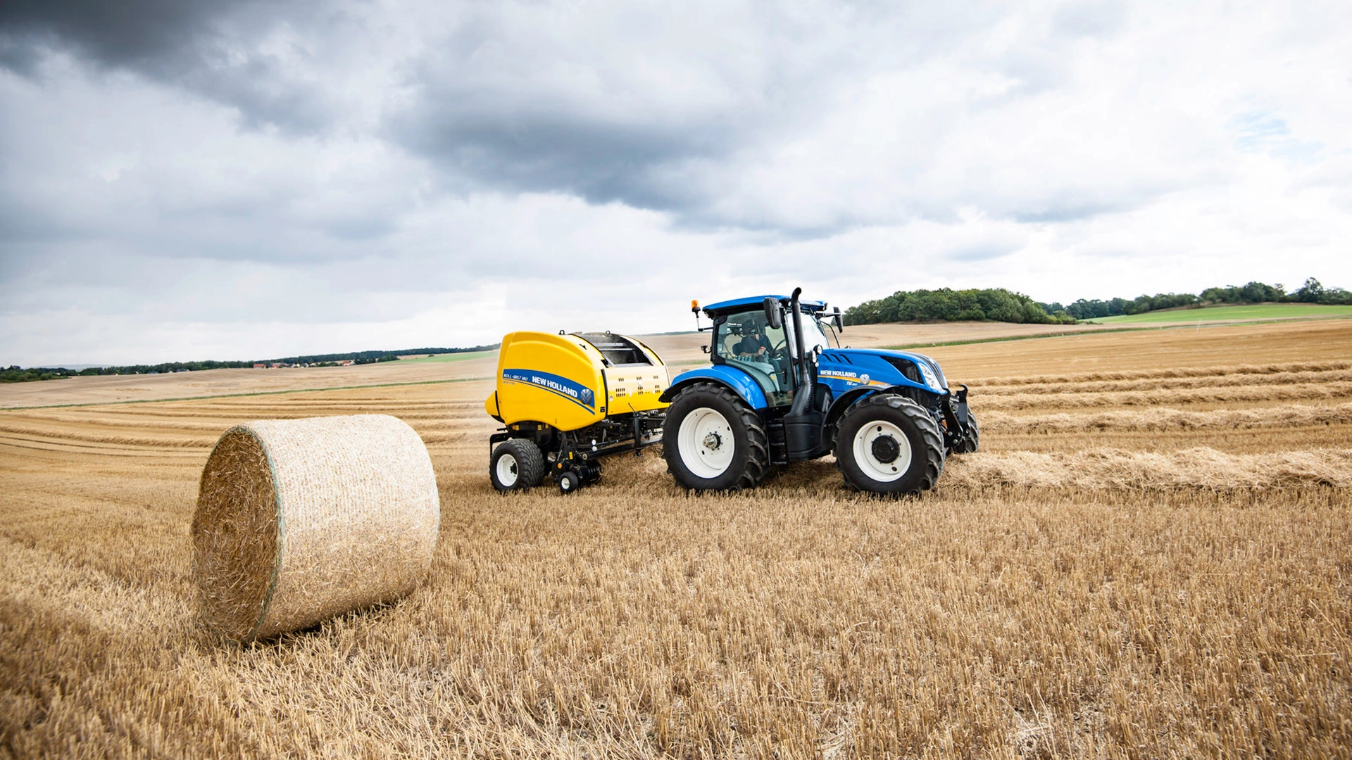 Tractor and Roll-Belt round baler combination actively bundling hay on the farmland