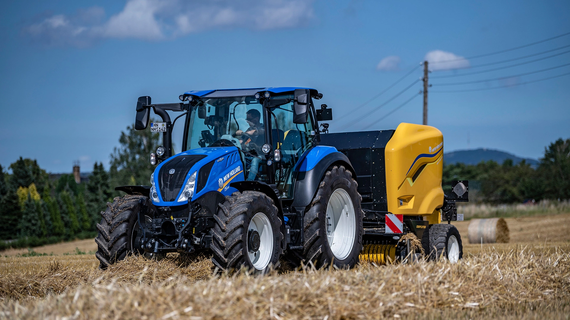 New Holland Tractor making round bales with Roll Bar 125 round baler.